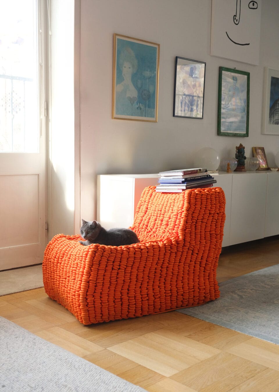 an orange chair made of knitted nylon rope, shown in a home with a cat sitting on it
