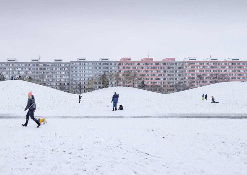 a photo in winter of people playing in a snowy park, with a huge residential complex in the background