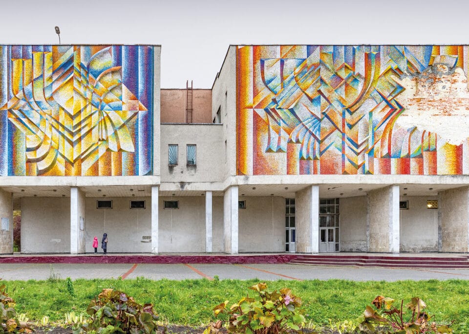 a blocky Soviet-era building with large facades and columns, with colorful modernist paintings on the flat planes