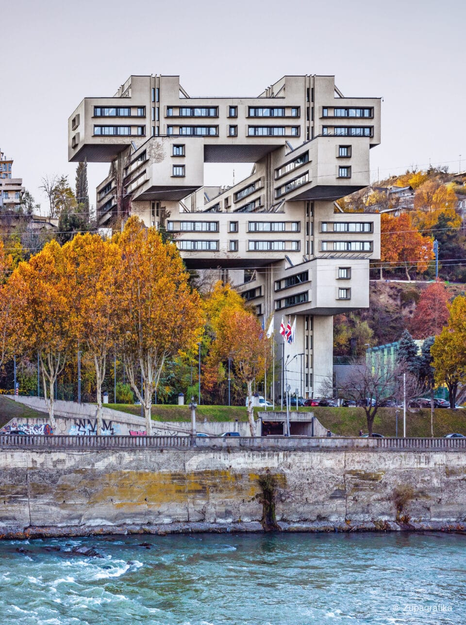 a multi-story Jenga-like brutalist construction amid autumnal trees