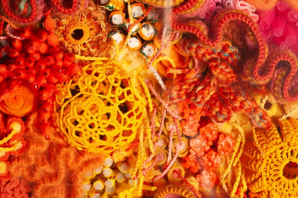a detail of a vibrant fiber work evoking corals, molds, and other organic forms