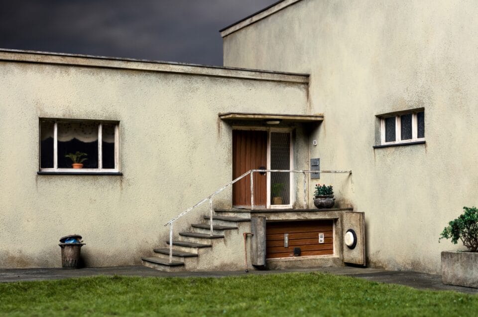 a photo of a miniature set showing the entrance to a building or house with another door tilted sideways and stuck under the stairwell as if it enters a parallel, sideways room