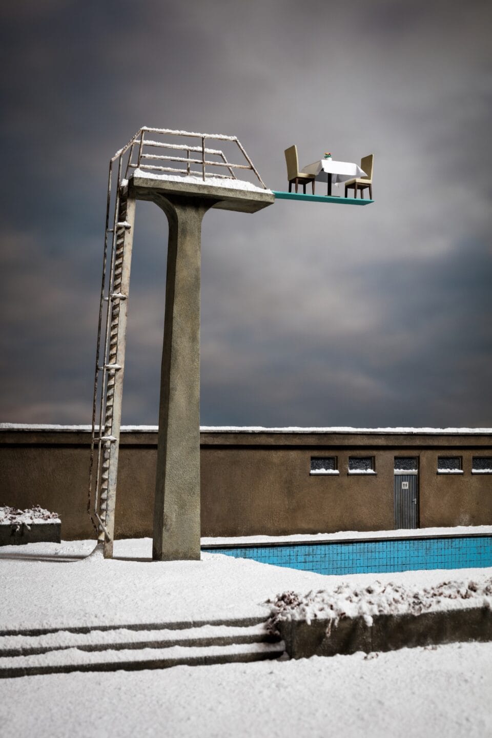 a photo of a miniature set showing a tall diving platform above a pool, covered in snow, with a table for two set up at the very top